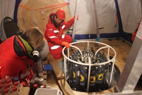 Scientists retrieving seawater from different depths using a carousel water sampler deployed through a hole in the sea ice.